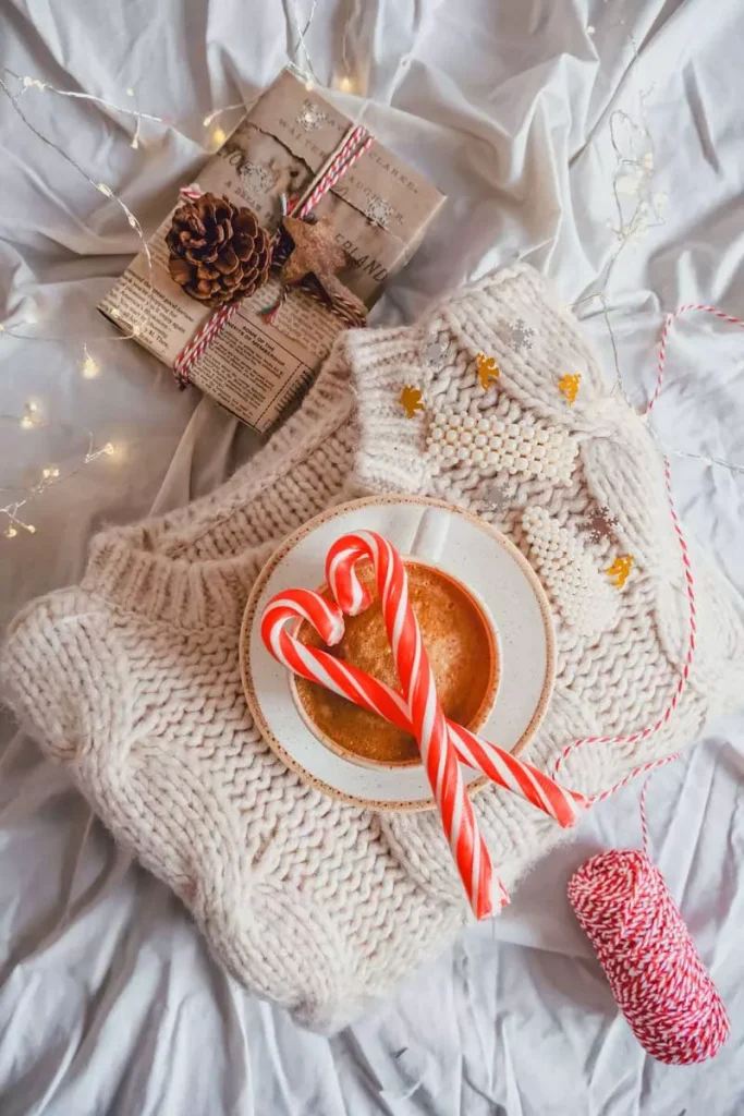 Sugar canes in a heart-shape laid on top of a festive knitted sweater, along with a paper-wrapped gift