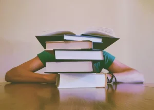 Student hiding face behind stacked books